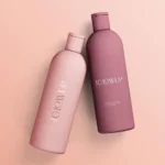 Two pink and mauve shampoo bottles labeled "GLOWUP" lie tilted on a pastel pink background, conveying elegance and modernity.